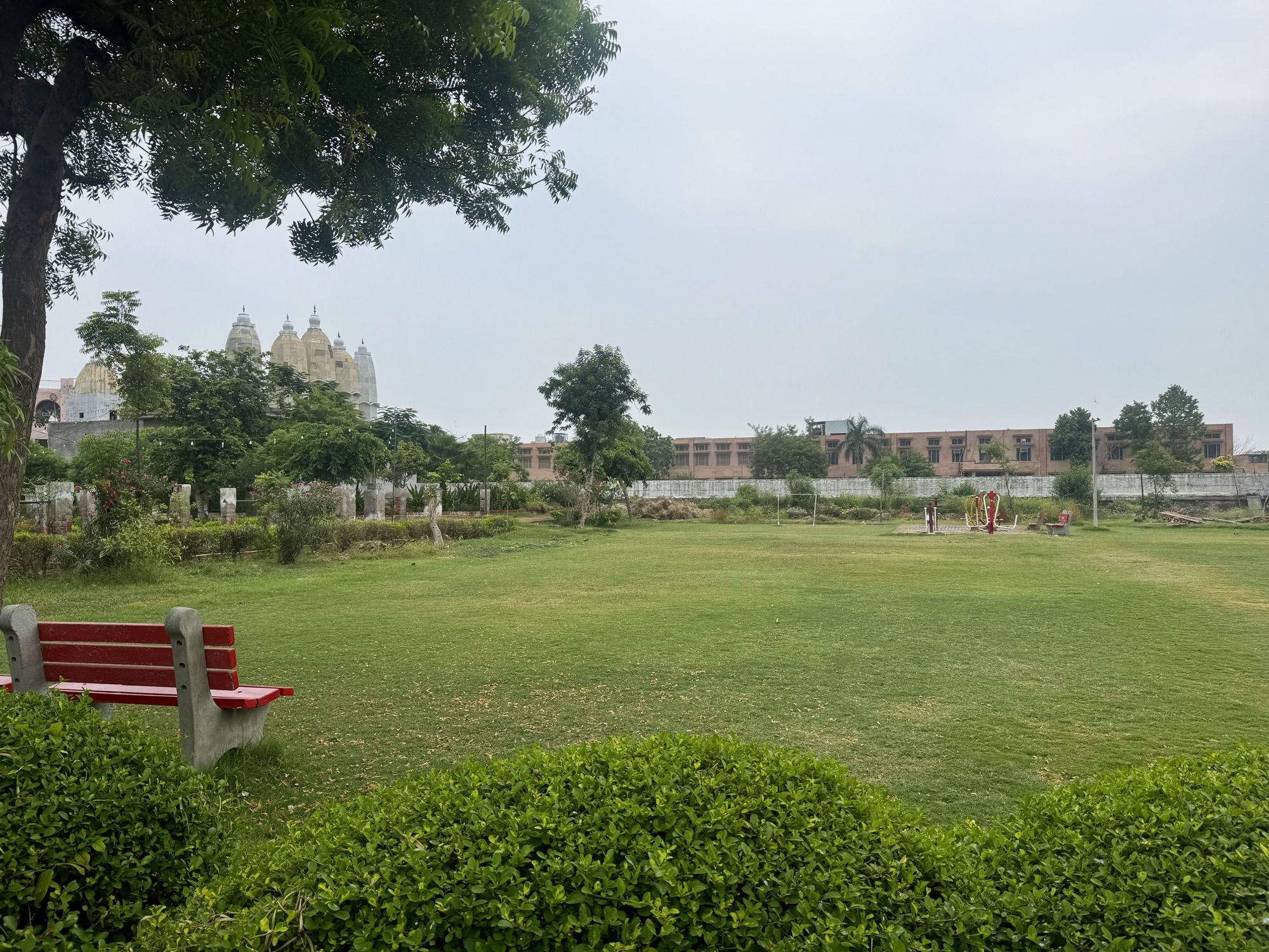 The lawn at Hansi Gita Bhawan with the open-air gym at its edge and the temple shikharas rising behind the trees