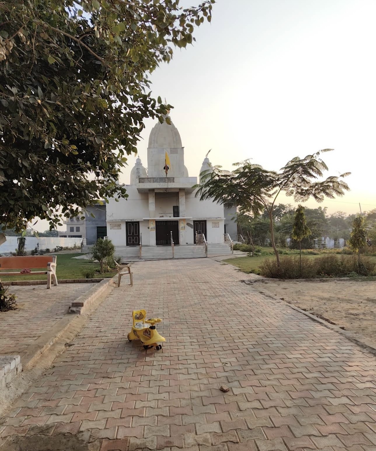 The brick approach to the temple at Hansi Gita Bhawan in the early morning, benches and young trees along one side and a child’s ride-on toy left on the path