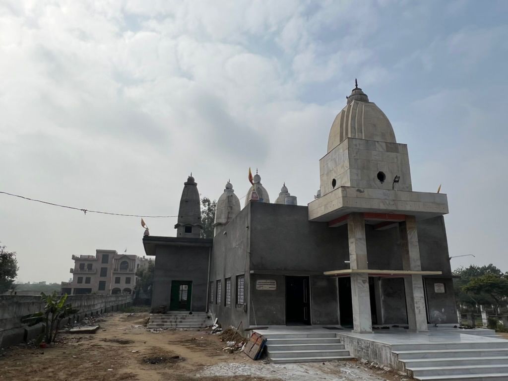 The new temple under construction at Hansi Gita Bhawan, its shikhara finished in bare grey concrete above three unframed doorways, the older white shrines standing behind it